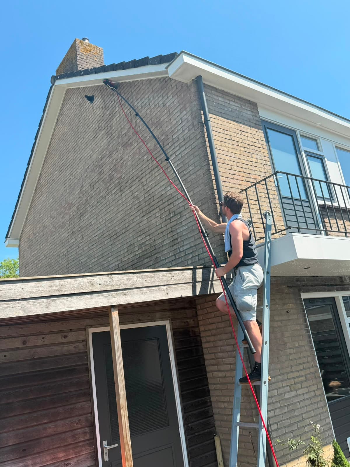 Medewerker van Madern reinigt vanaf een ladder de dakgoot en dakrand van een woning in Apeldoorn met een telescoopsteel