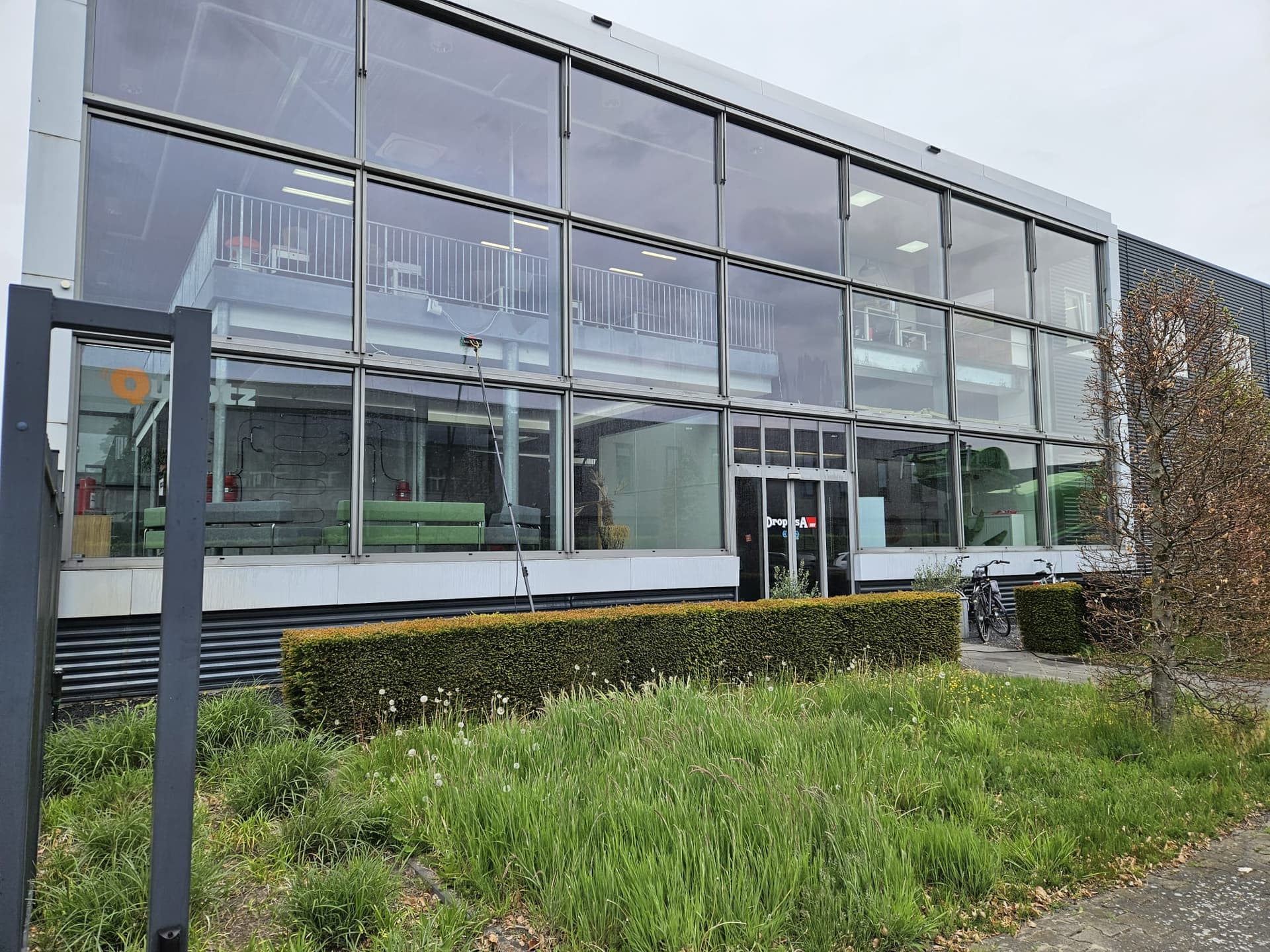 Glazenwasser Apeldoorn: watergevoede telescoopsteel van Madern tegen de glasgevel van een kantoorpand tijdens de glasbewassing