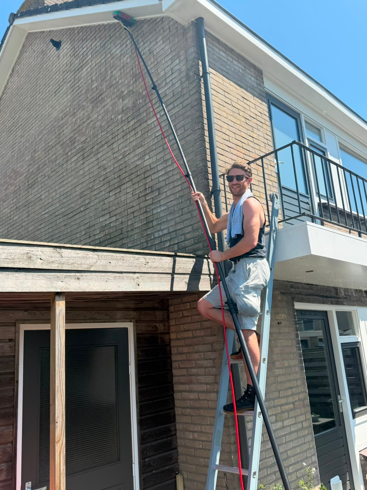 Glazenwasser van Madern wast vanaf een ladder de ramen en dakrand van een woning in Apeldoorn met een watergevoede telescoopsteel