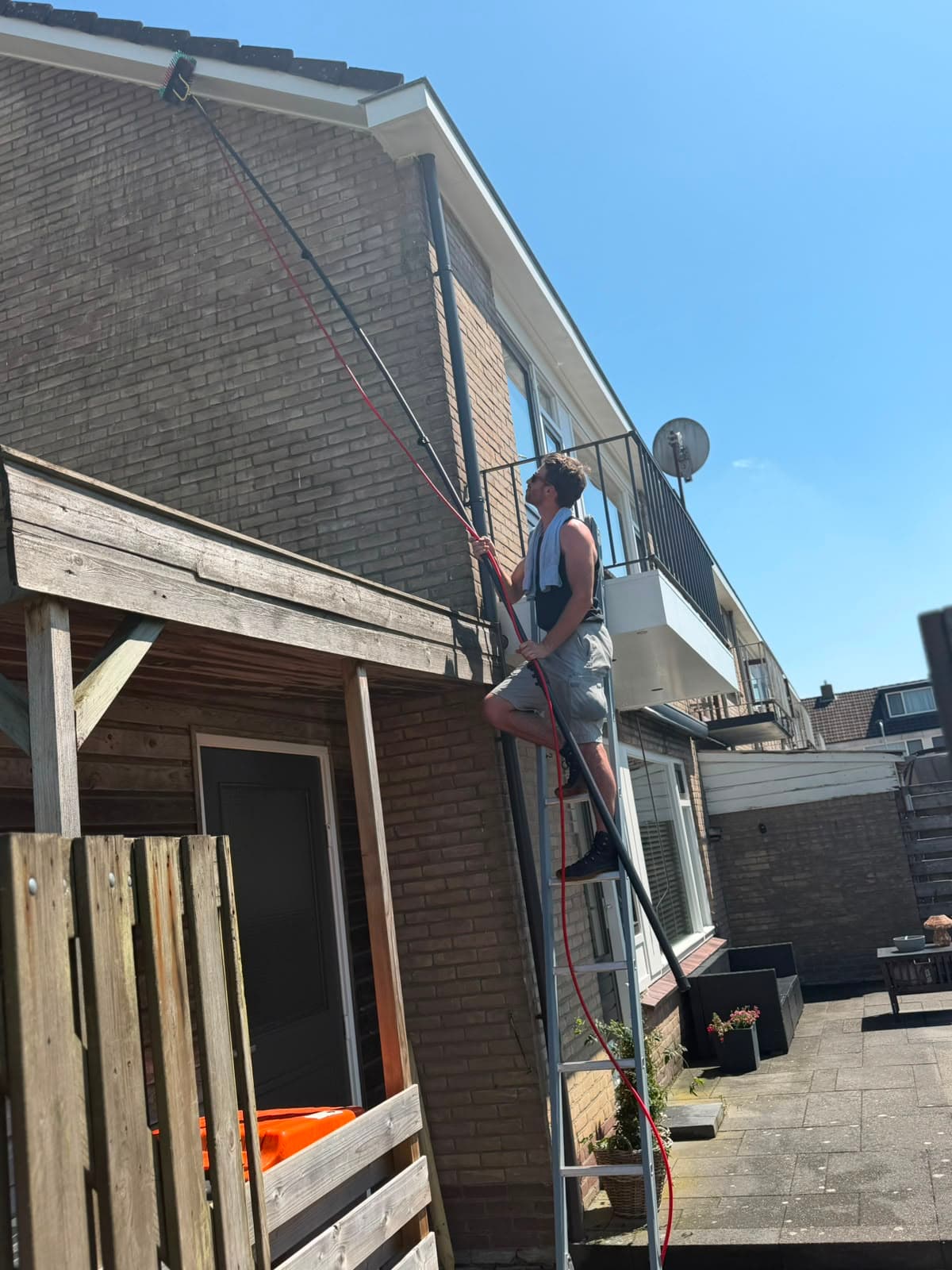 Dakgootreiniging bij een woning in Apeldoorn vanaf een ladder met telescoopsteel